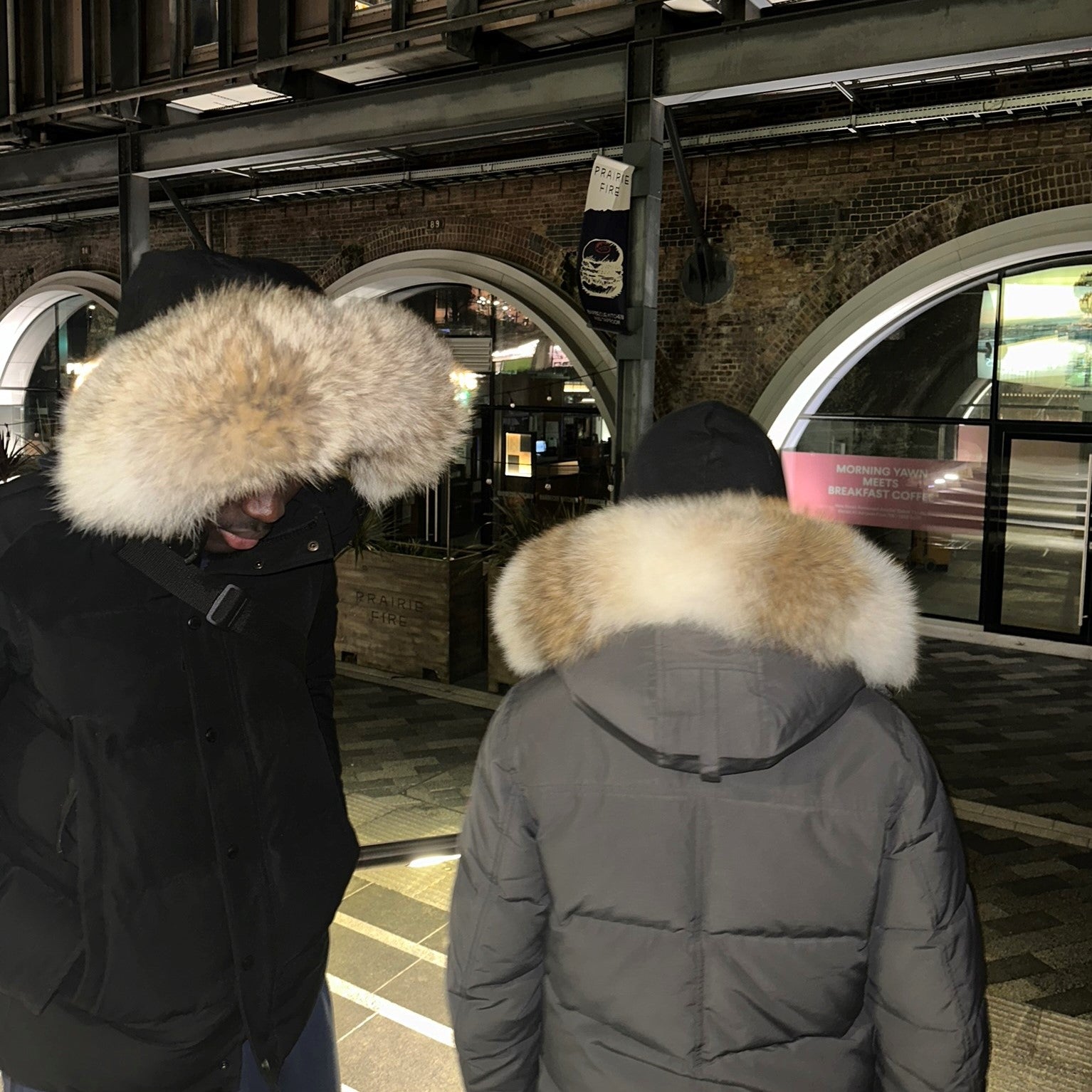Two men wearing Canada Goose Wyndham Parkas, one black with cream coyote fur hood replacement and one grey with milk brown fur trim